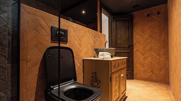 Un baño moderno con un inodoro negro, paredes de madera y un suelo con estampado tipo espiga.