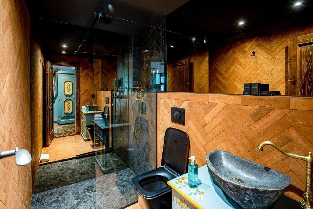 Un baño moderno con pared de madera estampada en espiga, un lavamanos de piedra y zona de ducha con mampara de vidrio.