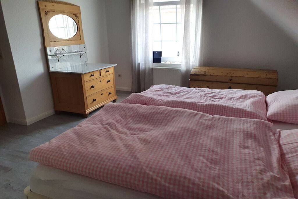 A bedroom with two beds, a wooden dresser, a mirror, and a window with curtains.
