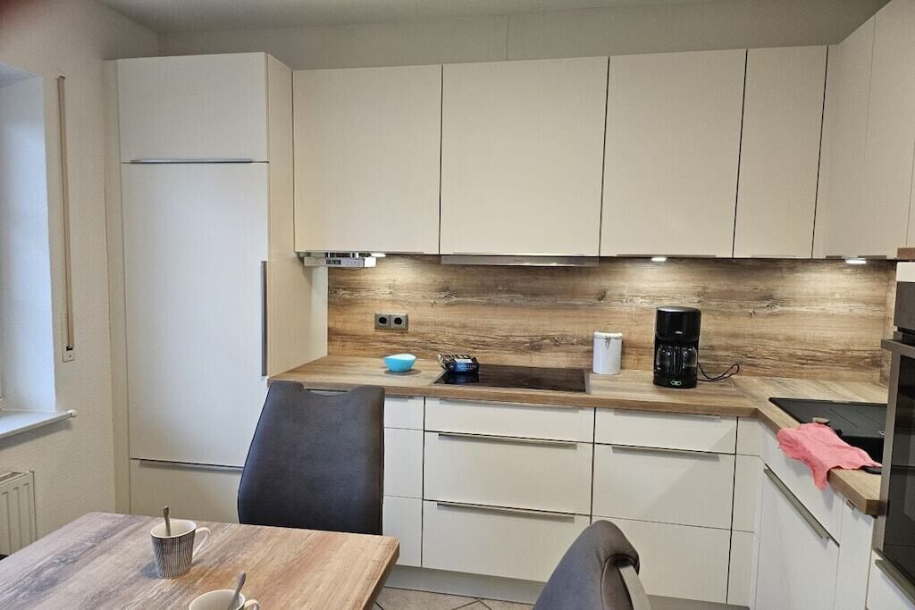 Ett modernt kök med vita skåp, en bänkskiva i trä och en kaffebryggare.