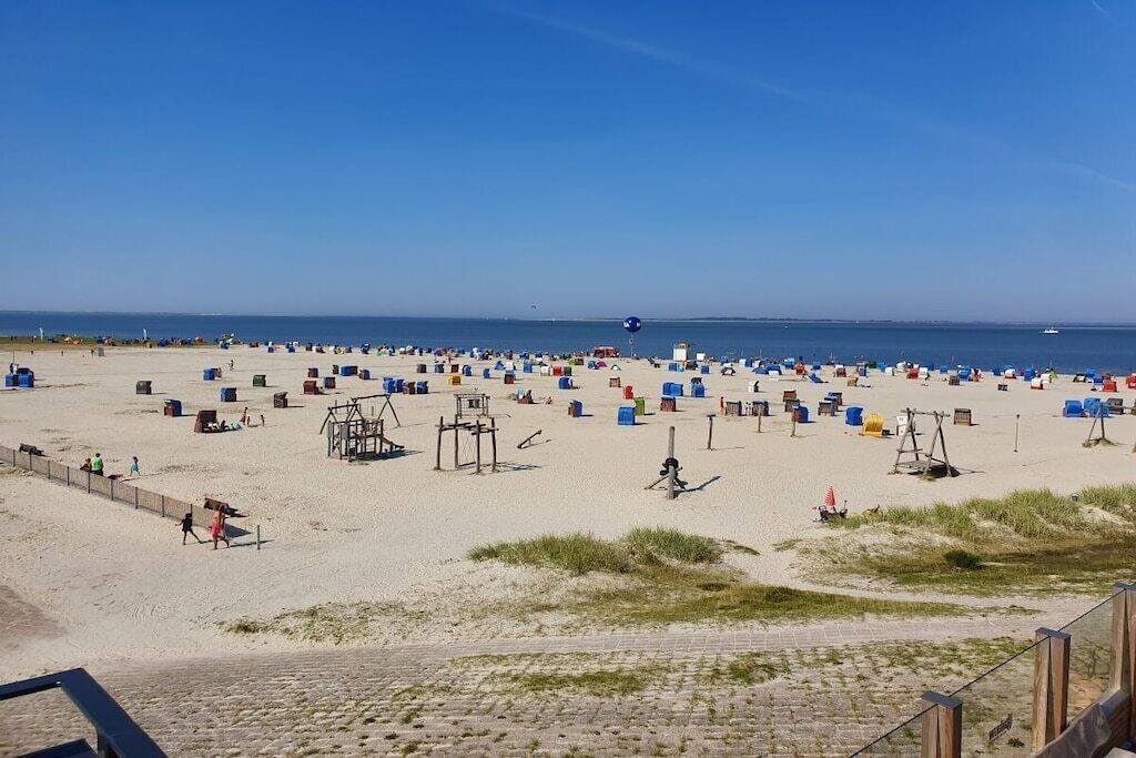 A beach with numerous sun loungers and beach chairs, a lifeguard tower, and a clear view of the sea.