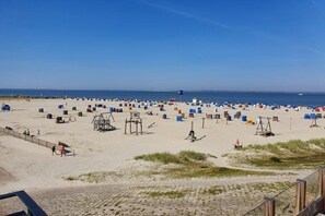 A beach with numerous sun loungers and beach chairs, a lifeguard tower, and a clear view of the sea. - Holiday home with 1 bedroom (Dornumersiel)