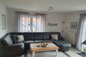 A modern living room with a sectional sofa, a coffee table, and a floor lamp. - Holiday home with 1 bedroom (Dornumersiel)