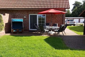 A brick building with a tiled roof, a patio with a table and chairs, and a red umbrella. - Holiday home with 1 bedroom (Dornumersiel)