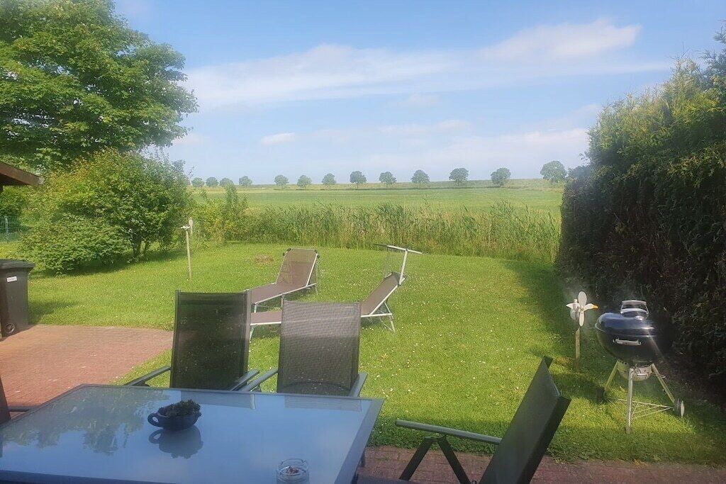 An outdoor seating area with a table and chairs, a barbecue grill, and a view of a grassy field.