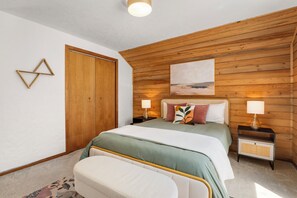 Ein Schlafzimmer mit Holzbalkendecke, einem Bett mit zwei Kissen, einem Nachttisch mit Lampe und einem Wandbild.