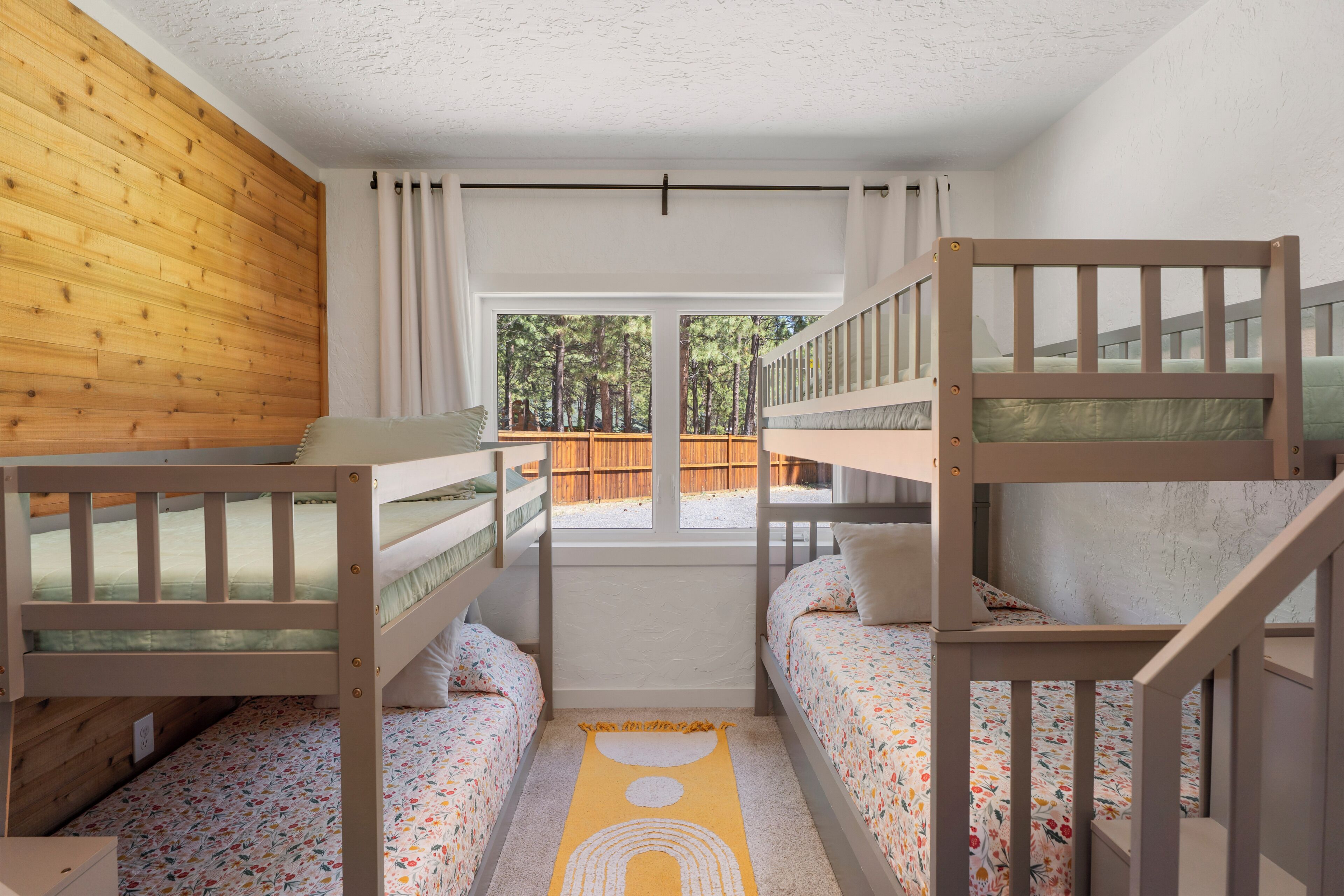 A room with bunk beds, a window with a view of trees, and a wooden wall.