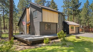 A modern two-story house with a wooden deck, a fenced yard, and a view of the surrounding forest. - Modern Tollgate Mountain Retreat (Sisters)