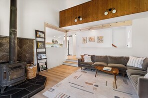 A modern living room with a stone fireplace, a sofa, a coffee table, and a bookshelf. - Modern Tollgate Mountain Retreat (Sisters)