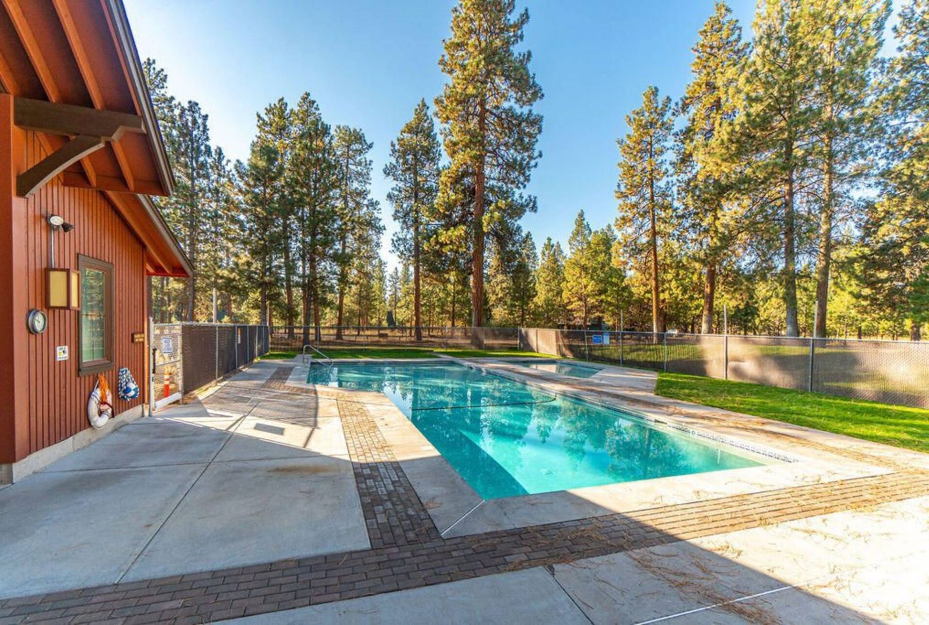 A swimming pool with a brick border, surrounded by a wooden deck and tall trees.