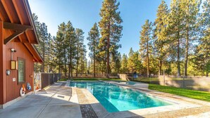 A swimming pool with a brick border, surrounded by a wooden deck and tall trees. - Modern Tollgate Mountain Retreat (Sisters)