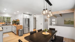 A modern kitchen with stainless steel appliances, a dining area with a dark wood table, and a view of the outdoors. - Modern Tollgate Mountain Retreat (Sisters)