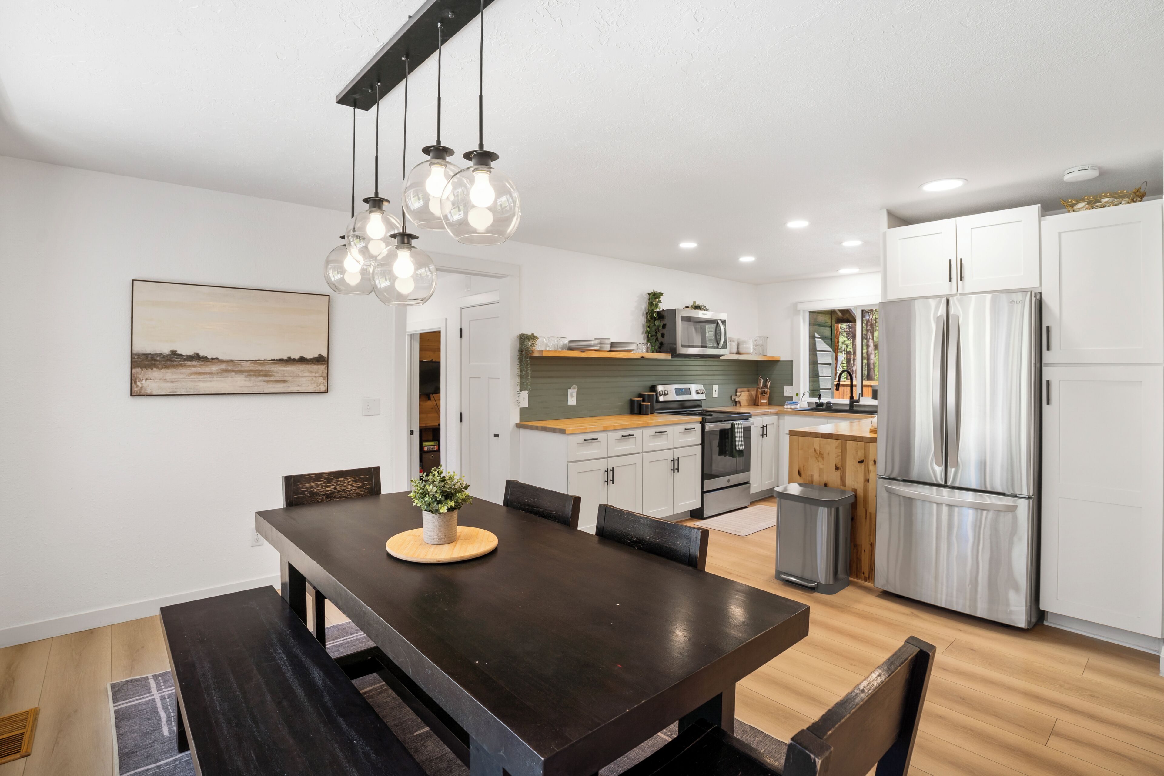A modern kitchen with white cabinets, a stainless steel refrigerator, and a dining area with a dark wooden table and chairs.