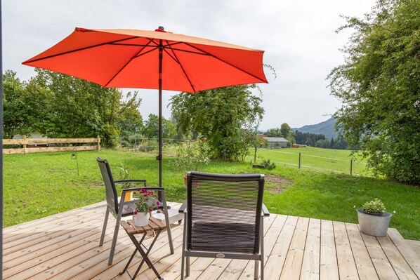 An outdoor deck with a red umbrella, two chairs, and a table with a potted plant.