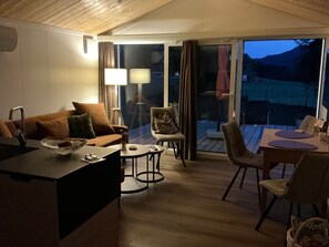 A modern interior with a sofa, chairs, a dining table, and a view through a glass door. - Tiny Home "Auszeit" with Mountain View, Wi-Fi, and Air Conditioning (Scheidegg)