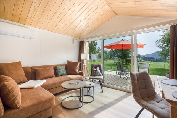 A modern living room with a wooden ceiling, a sofa, a coffee table, and a view of a deck with outdoor furniture.