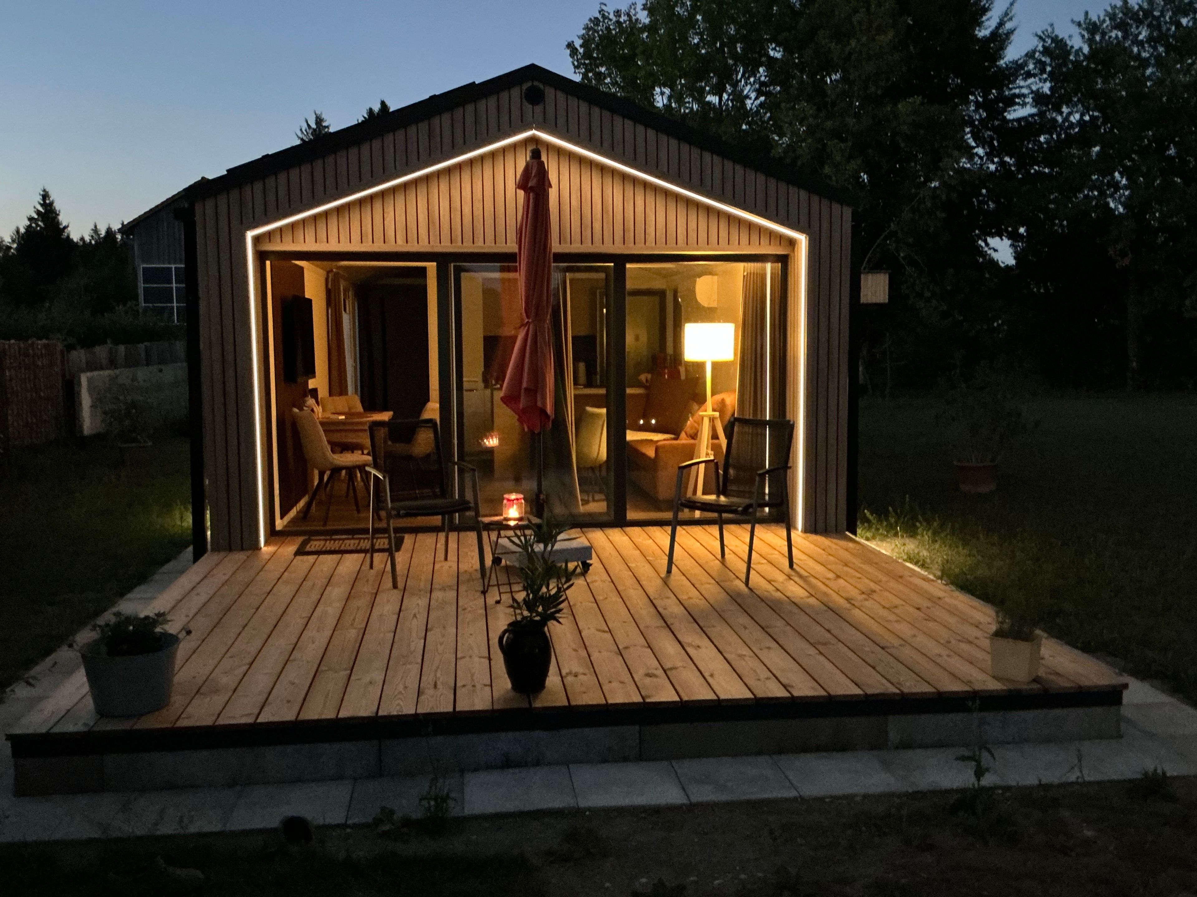 A wooden deck with a glass door leading to an interior space, a potted plant, and a table with a lamp.