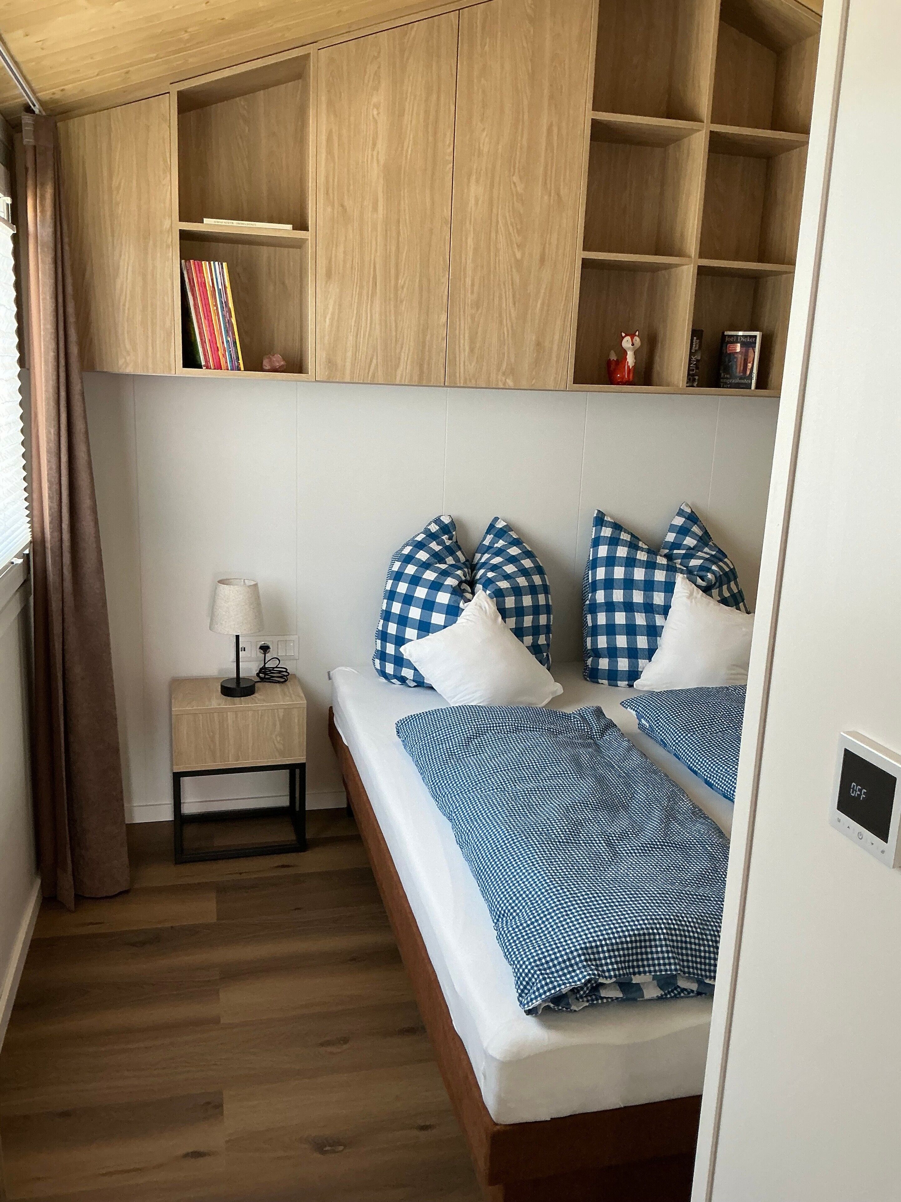 A bedroom with two beds, a bedside table with a lamp, and a wooden wardrobe with shelves.