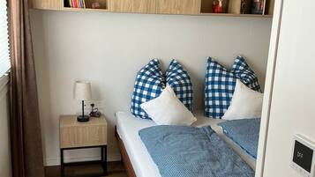 A bedroom with two beds, a bedside table with a lamp, and a wooden wardrobe with shelves.