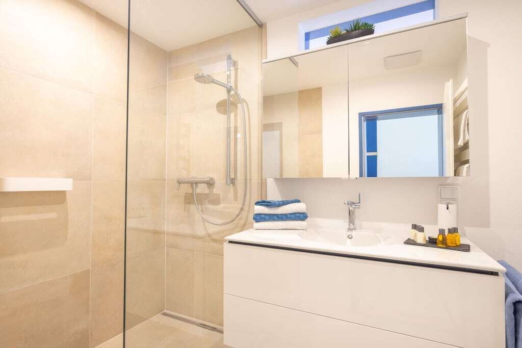 A modern bathroom with a glass-enclosed shower, a white vanity with a mirror, and a towel rack.