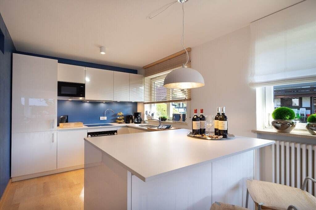 Een moderne keuken met witte kasten, een centraal eiland en een hanglamp.
