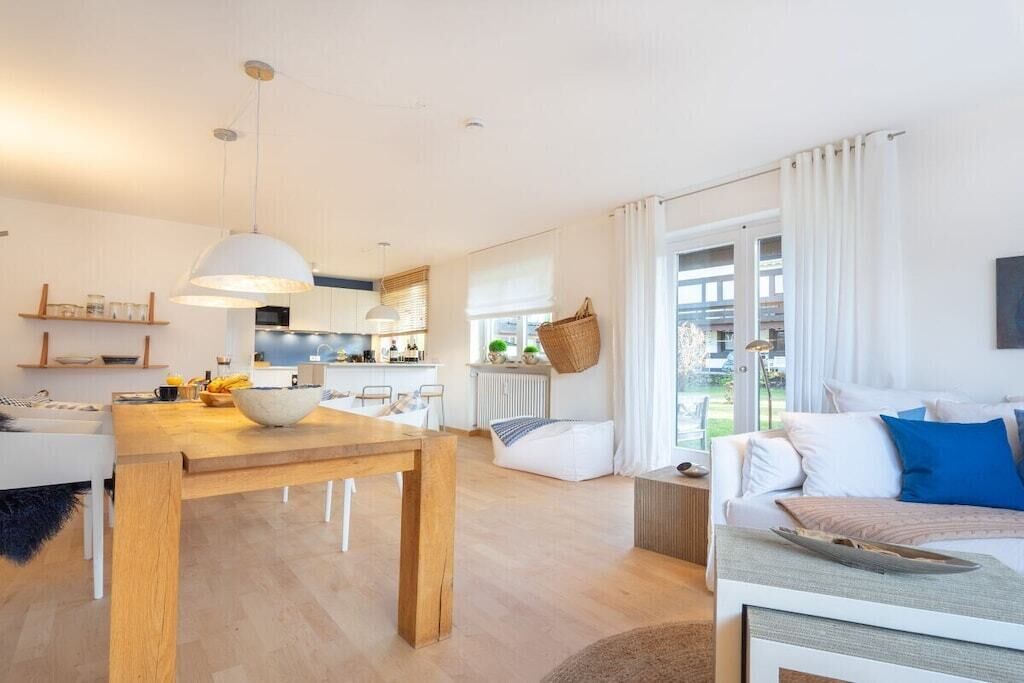 Um espaço de estar moderno com uma mesa de jantar de madeira, um sofá e uma cozinha.