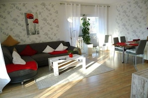 Ein Wohnzimmer mit Sofa, Couchtisch, Esstisch, Stühlen und einer Topfpflanze.