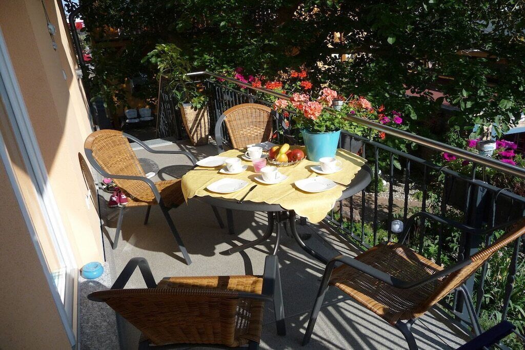 A balcony with a table set for two, surrounded by wicker chairs, and a potted plant with flowers.