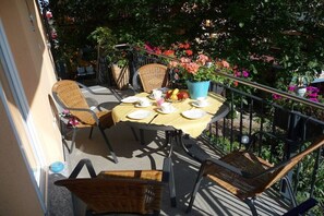 Ein Balkon mit Tisch für zwei Personen, umgeben von Korbstühlen und einem Blumentopf mit Blumen.