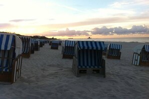 Strandstühle reihen sich an einem sandigen Strand entlang, mit Blick auf den Ozean und einem Sonnenuntergang im Hintergrund.