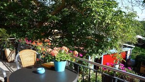 Ein runder Tisch mit einer blauen Schüssel, umgeben von Korbstühlen, auf einem Balkon mit Metallgeländern.
