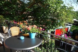 Ein runder Tisch mit einer blauen Schüssel, umgeben von Korbstühlen, auf einem Balkon mit Metallgeländern.
