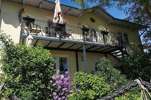 Ein zweistöckiges Gebäude mit einem Balkon, Außenbestuhlung und Kübelpflanzen.