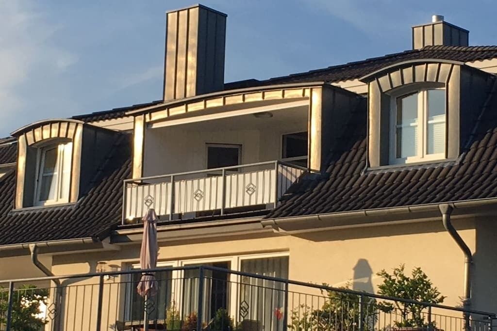 Ein Wohngebäude mit mehreren Balkonen, einem Schornstein und einem Fenster mit Vorhängen.