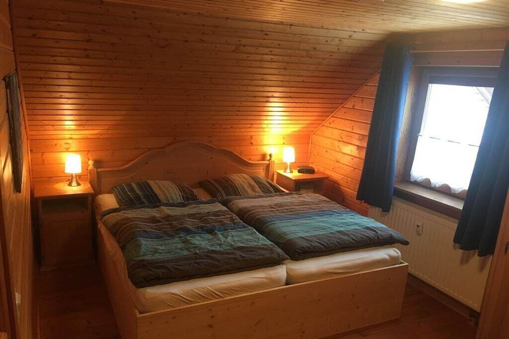 A wooden-paneled room with a bed, two bedside tables, and a window with curtains.
