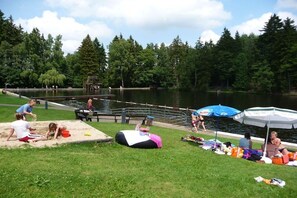 Ein Park am Seeufer mit einem Sandspielbereich, Picknicktischen und Sonnenschirmen.
