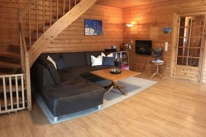 A cozy cabin interior with a wooden staircase, a sectional sofa, a small table, and a television. - Holiday home with 2 bedrooms (Hasselfelde-Rotacker)