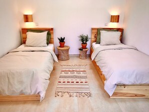 Ein Doppelzimmer mit zwei Betten, jeweils mit einem Holz-Kopfteil, weißer Bettwäsche und je einer Wandlampe.
