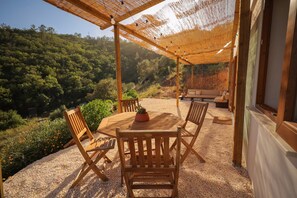 Ein Holz-Sitzbereich im Freien mit Tisch und Stühlen, einem Blumentopf und Blick auf einen bewaldeten Hügel.
