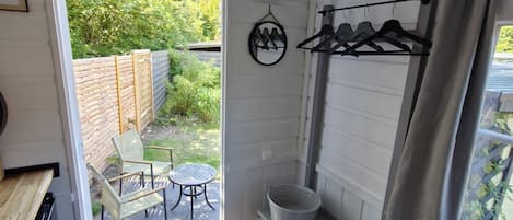Une pièce de taille modeste, avec un banc en bois, une petite table, un porte-vêtements suspendu et une fenêtre avec des rideaux.