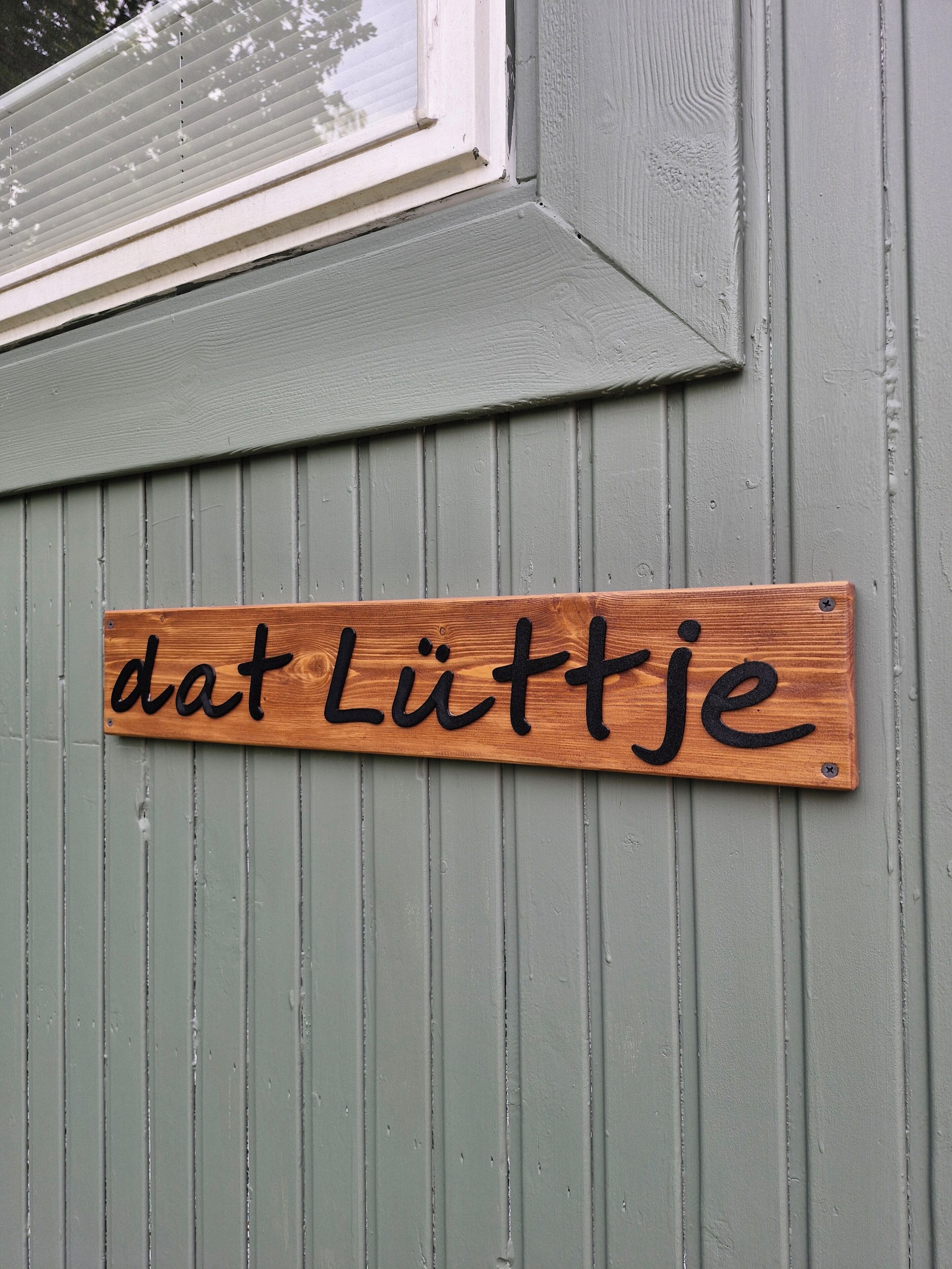 Une enseigne en bois portant l’inscription « dat Lüttje » est fixée à un mur.