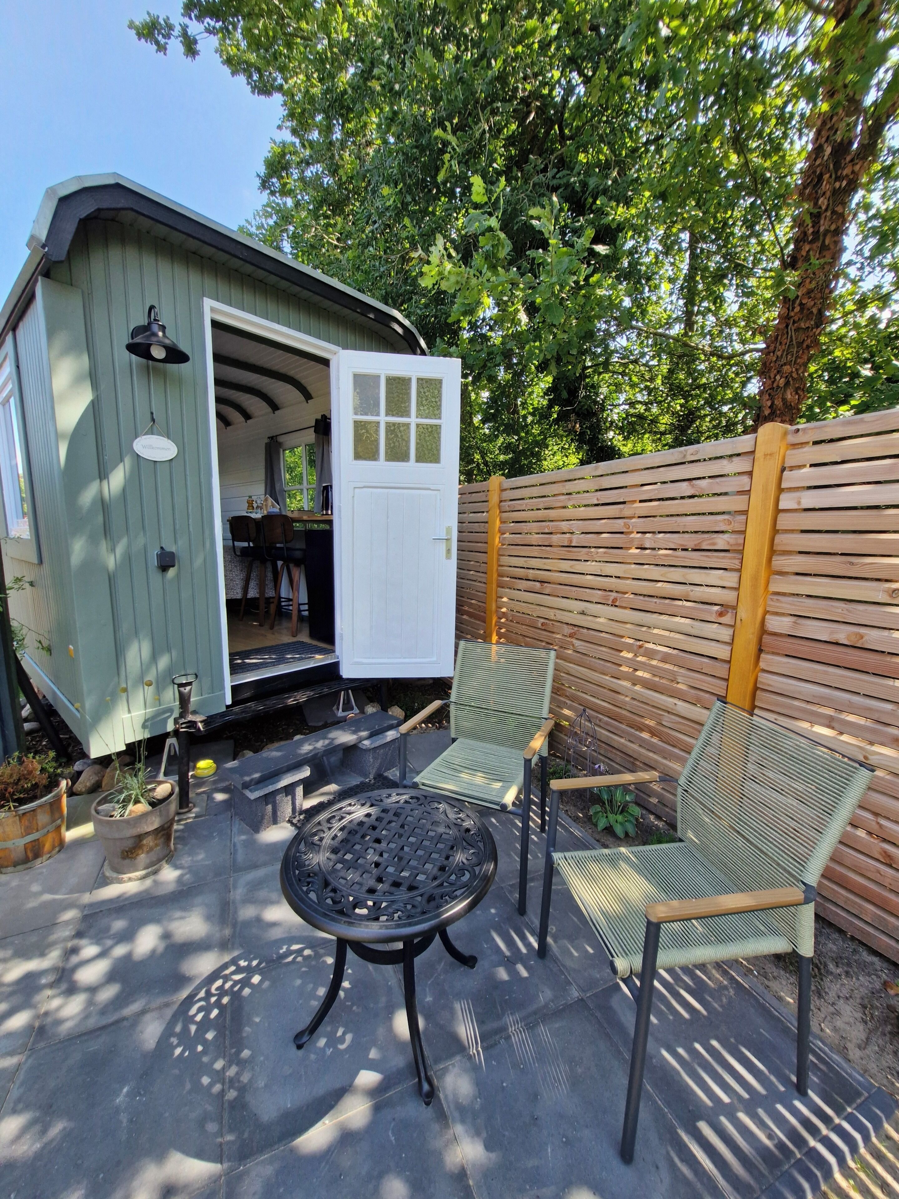 A patio with a metal table and two chairs, a shed with a door open, and a wooden fence.