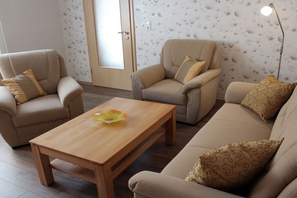 Uma sala de estar com sofá, duas poltronas, mesa de centro de madeira e um abajur.