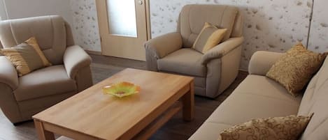 Uma sala de estar com sofá, duas poltronas, mesa de centro de madeira e um abajur.