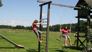 Un conjunto de juegos de madera con un columpio, tobogán y una pequeña estructura en un campo cubierto de césped.