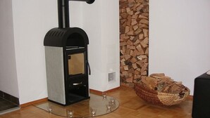 Una estufa de leña con tapa de vidrio, chimenea y espacio para almacenar leña.