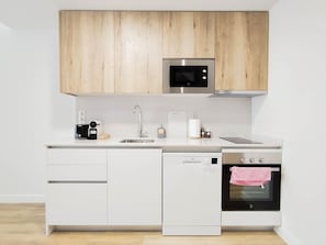 Eine moderne Küche mit weißen Schränken, einer Mikrowelle, einer Kaffeemaschine, einem Spülbecken, einem Geschirrspüler und einem Backofen.