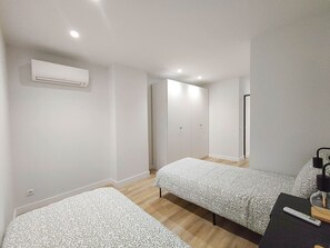Ein Schlafzimmer mit zwei Betten, einem Kleiderschrank, einem Schreibtisch mit Lampe und einer Klimaanlage.
