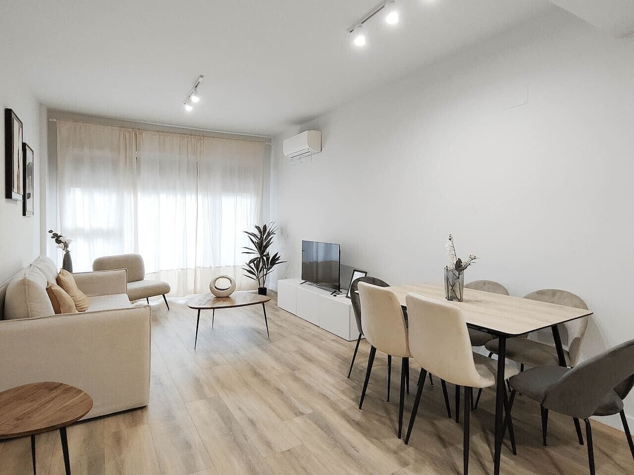 Una sala moderna con sofá, mesa de comedor, sillas, mesa de centro y televisor.