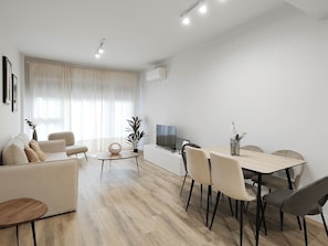 Uma sala de estar moderna com sofá, mesa de jantar, cadeiras, mesinha de centro e televisão.